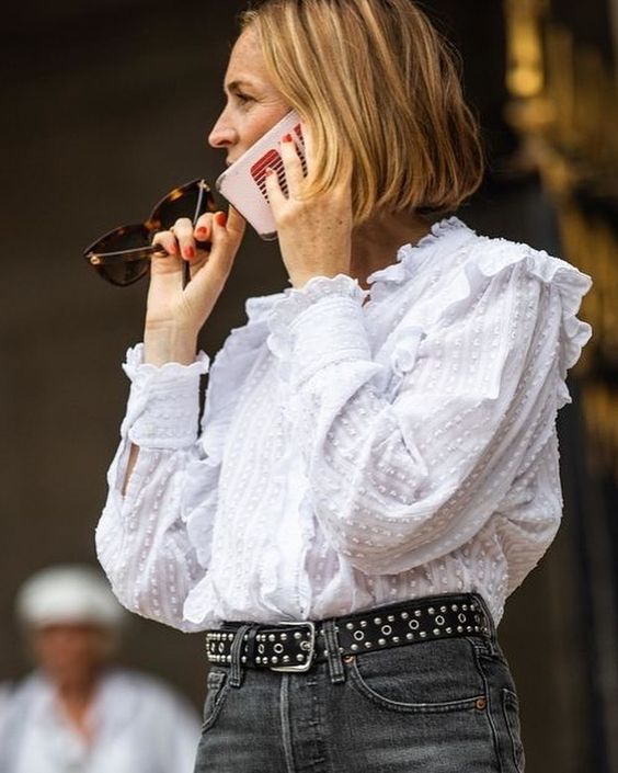 The woman is wearing a white blouse with grey jeans and a black studded belt.